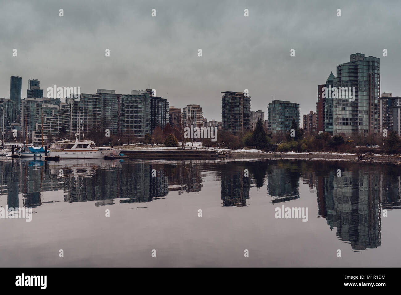 Vista del porto e Vancouver (BC, Canada) città di grattacieli con riflessi nell'acqua in un nuvoloso giorno d'inverno. Foto Stock