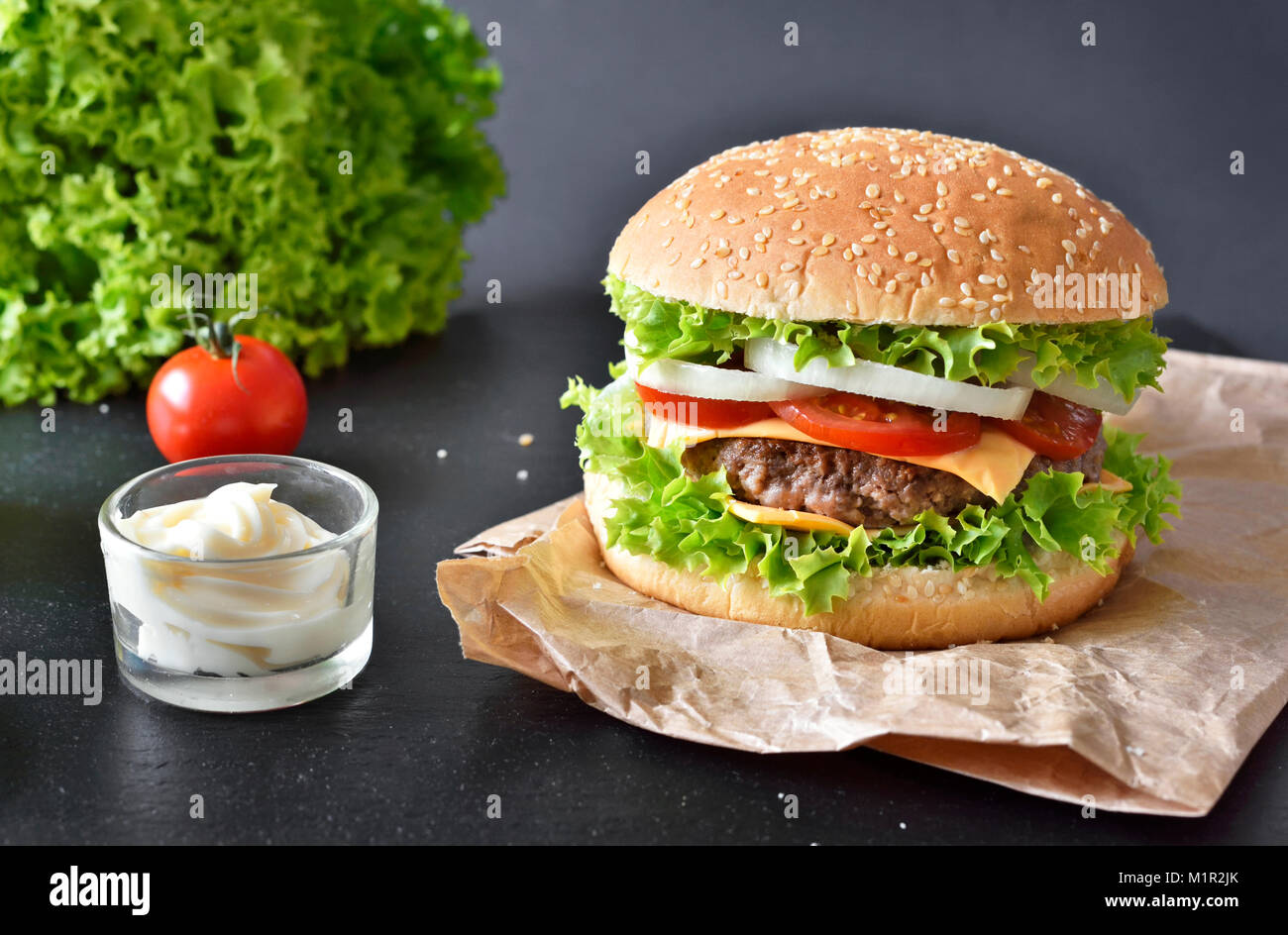 Hamburger freschi, hamburger o Cheeseburger con ketchup e maionese, cipolle e insalata. Deliziosi burger su una piastra di ardesia. Il fast food dello sfondo. Foto Stock