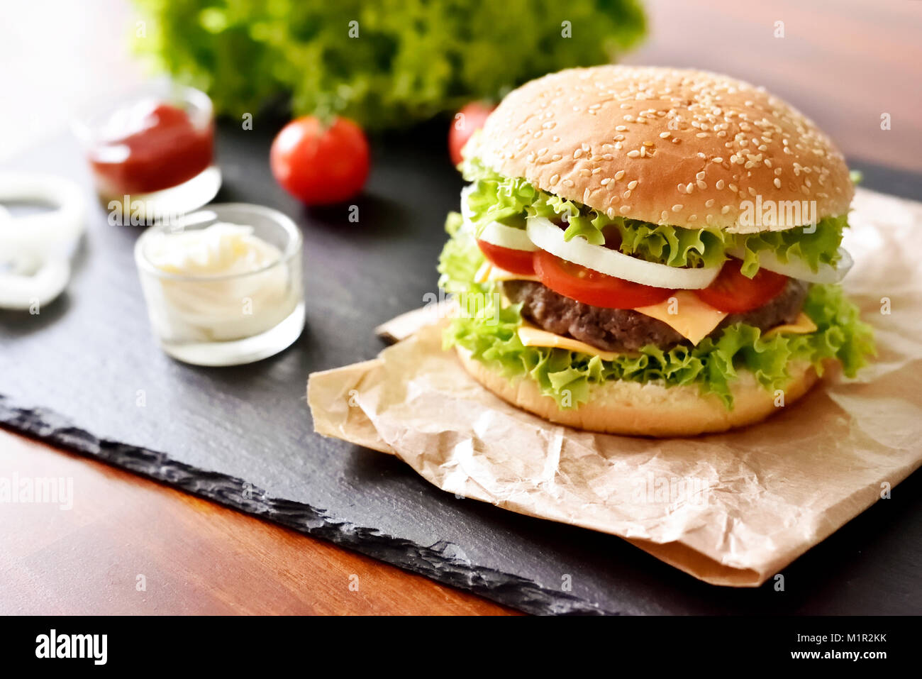 Hamburger freschi, hamburger o Cheeseburger con ketchup e maionese, cipolle e insalata. Deliziosi burger su una piastra di ardesia. Il fast food dello sfondo. Foto Stock