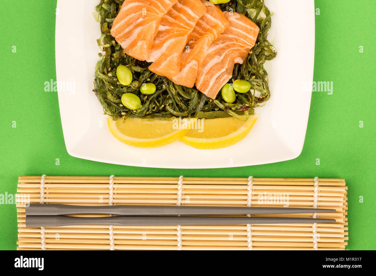 In stile giapponese sashimi di salmone su un letto di alghe sottaceto insalata e fagioli Edamame sfondo verde Foto Stock