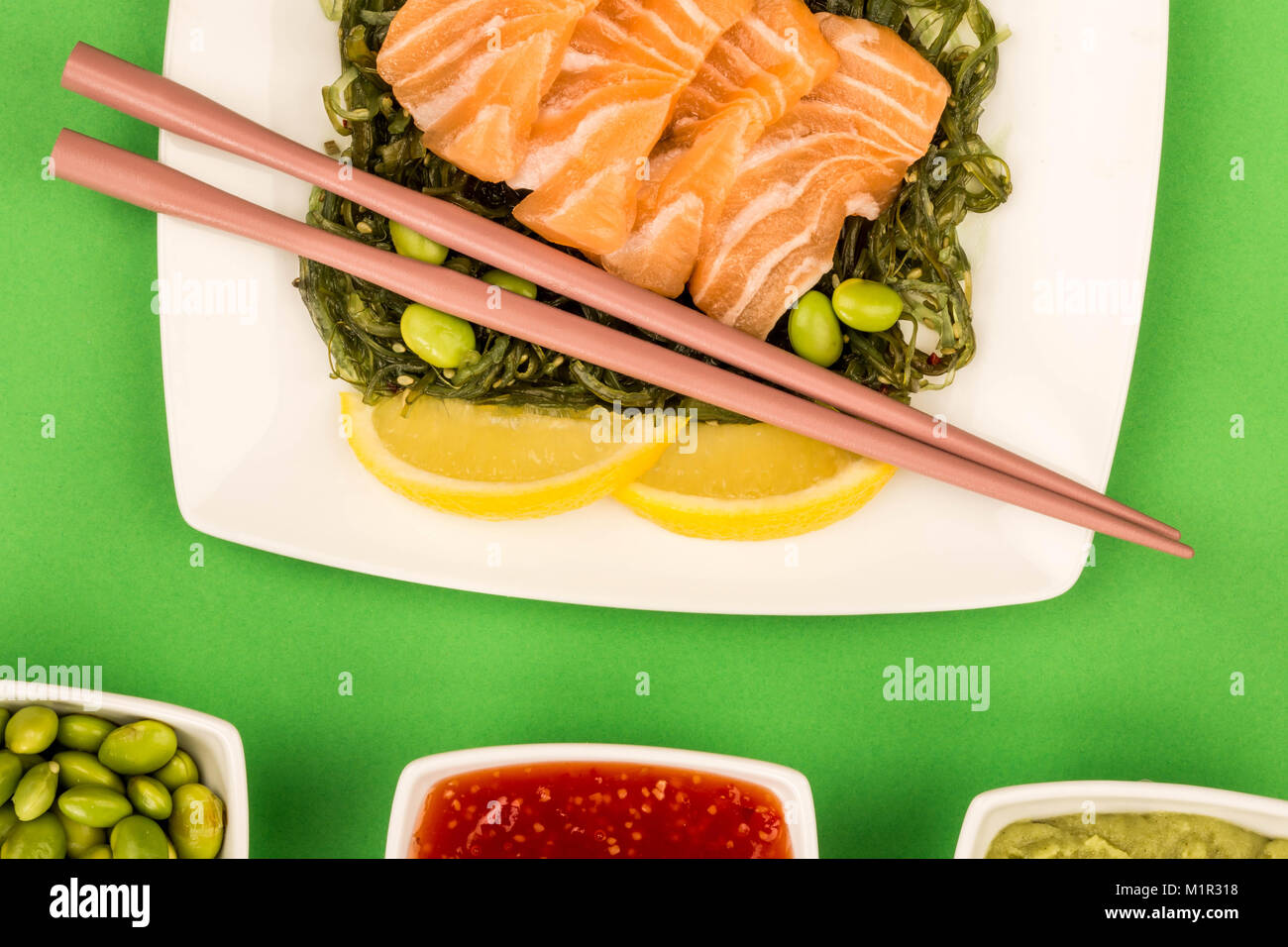 In stile giapponese sashimi di salmone su un letto di alghe sottaceto insalata e fagioli Edamame sfondo verde Foto Stock