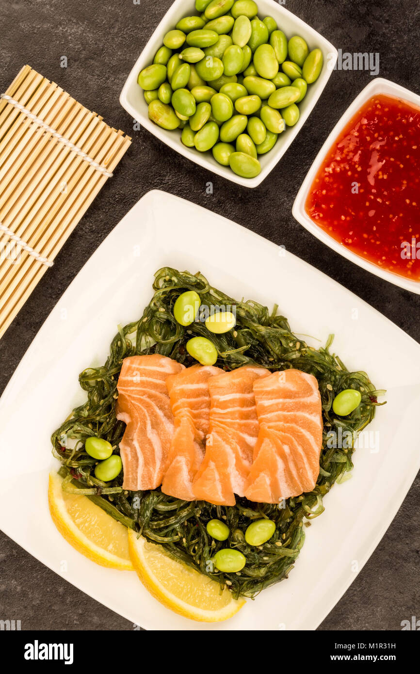 In stile giapponese sashimi di salmone su un letto di alghe sottaceto insalata e fagioli Edamame contro uno sfondo nero Foto Stock
