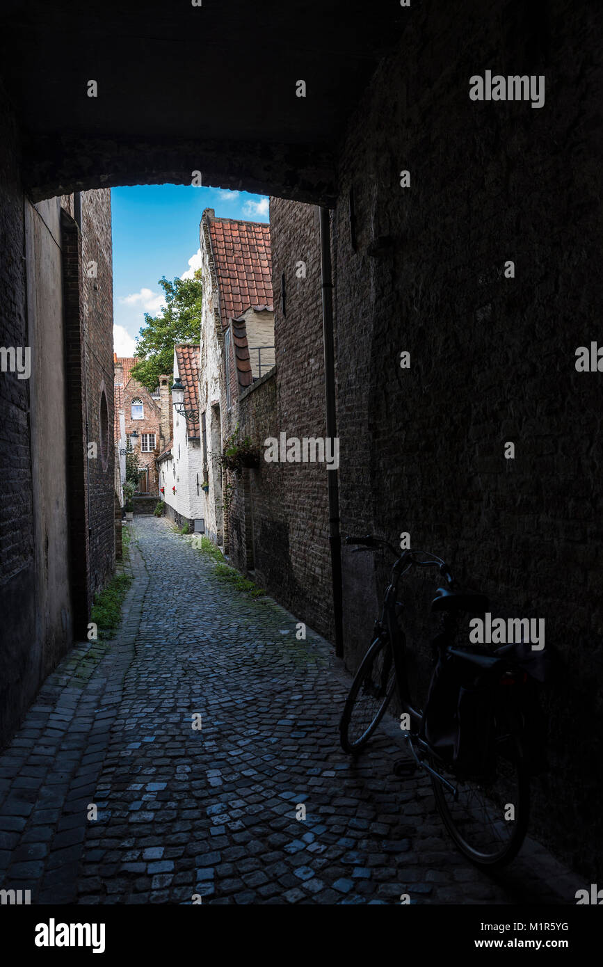 Prospettica di una strada stretta con vecchie case e una bicicletta parcheggiata in un vecchio centro storico della città medievale di Bruges, Belgio Foto Stock