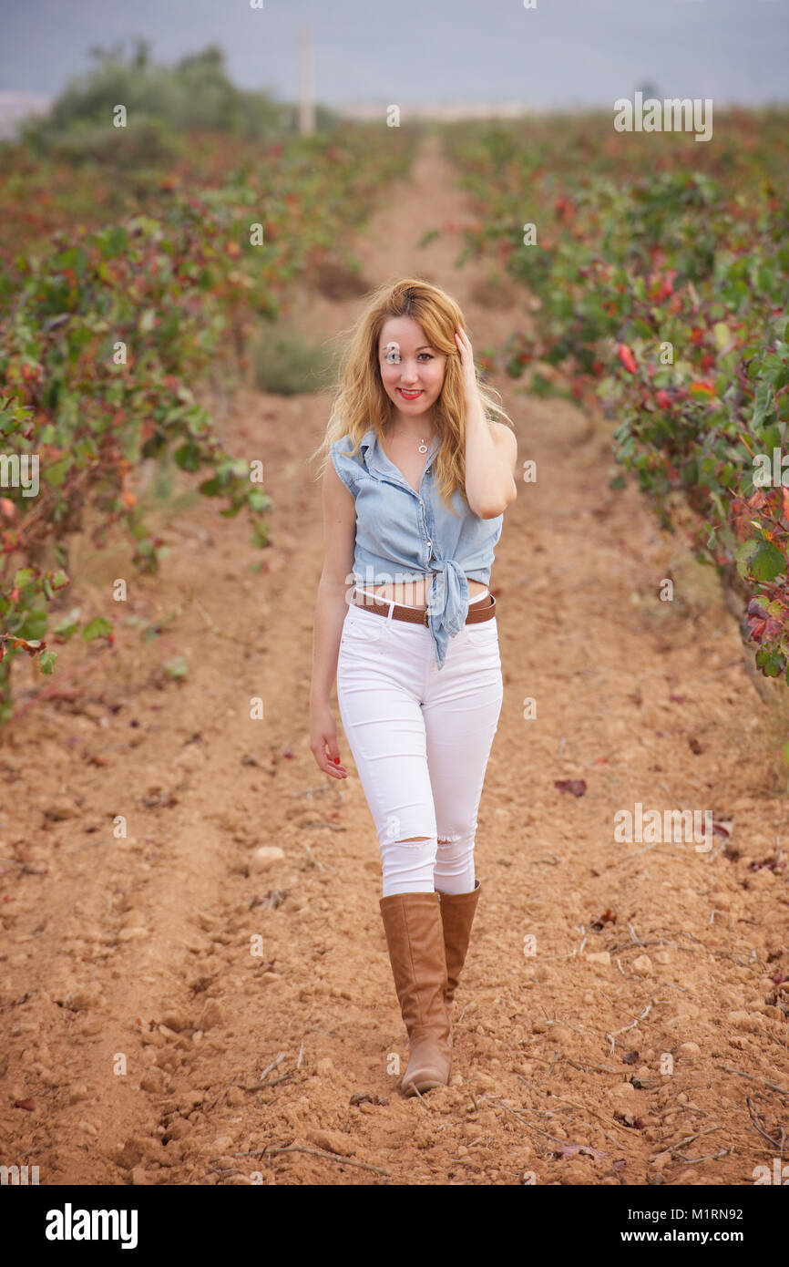 Bella ragazza che indossa jeans stretti e stivali nei pressi di un vigneto Foto Stock
