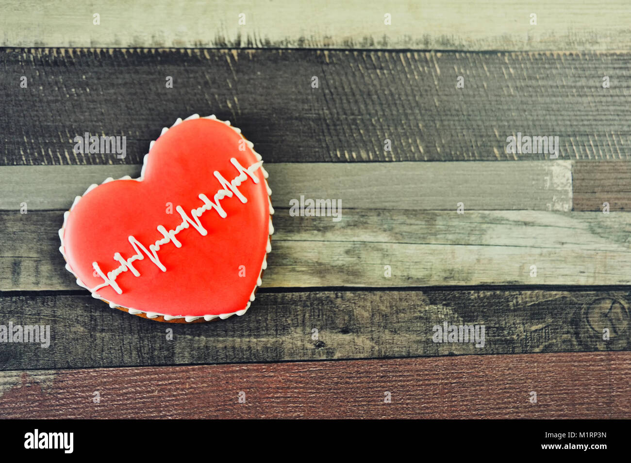 Gingerbread a forma di cuore decorata con smalto rosso e un modello sotto forma di un cardiogram su uno sfondo di legno. Foto Stock