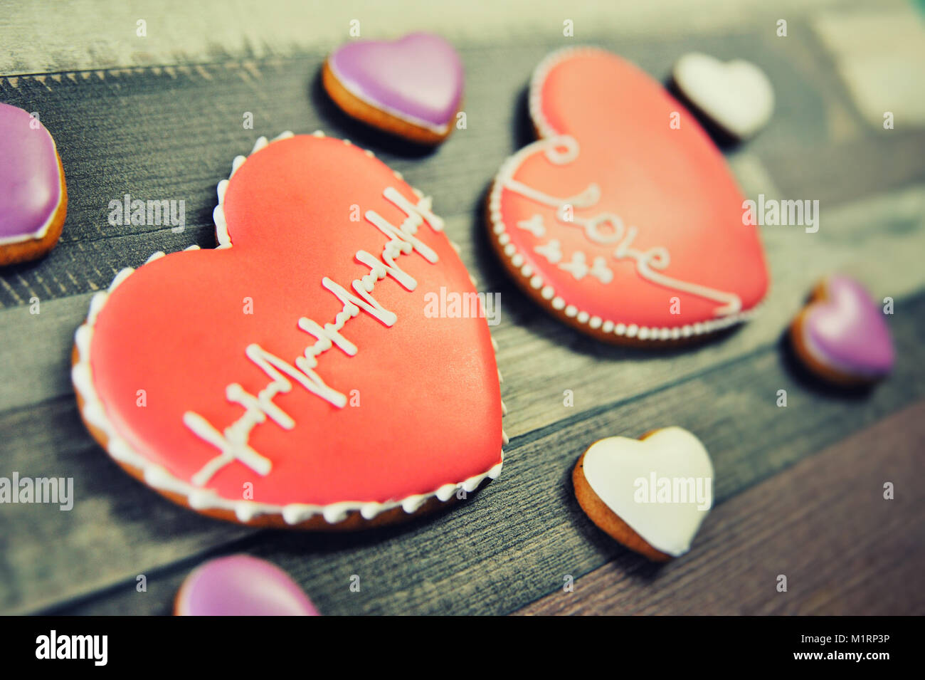 Gingerbread a forma di cuore decorata con smalto rosso e un modello sotto forma di un cardiogram su uno sfondo di legno. Foto Stock