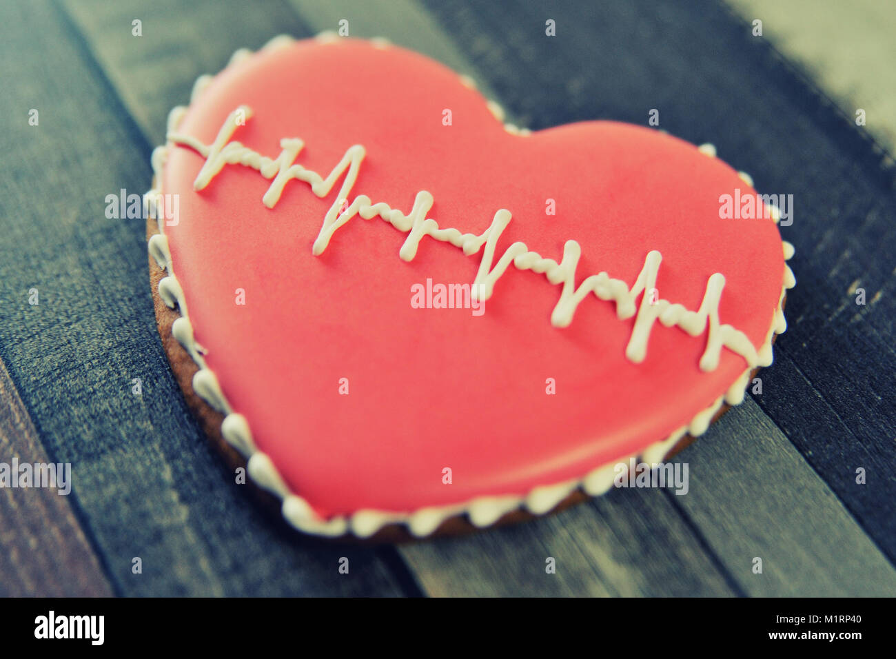 Gingerbread a forma di cuore decorata con smalto rosso e un modello sotto forma di un cardiogram su uno sfondo di legno. Foto Stock