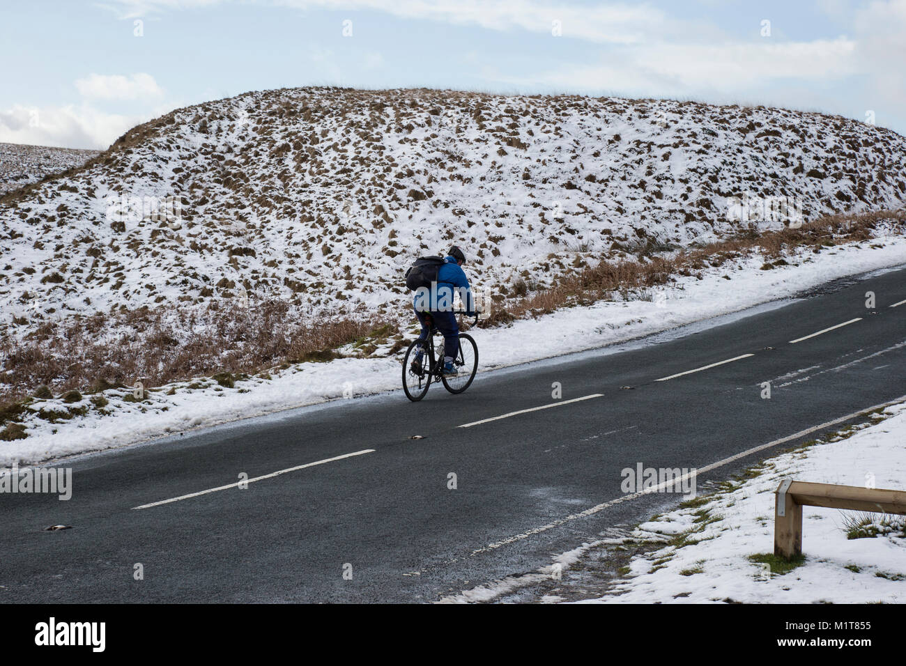 Ciclista solitario in condizioni nevose pedalando su una collina ai Yorkshire Moors sopra Marsden nel West Yorkshire Foto Stock