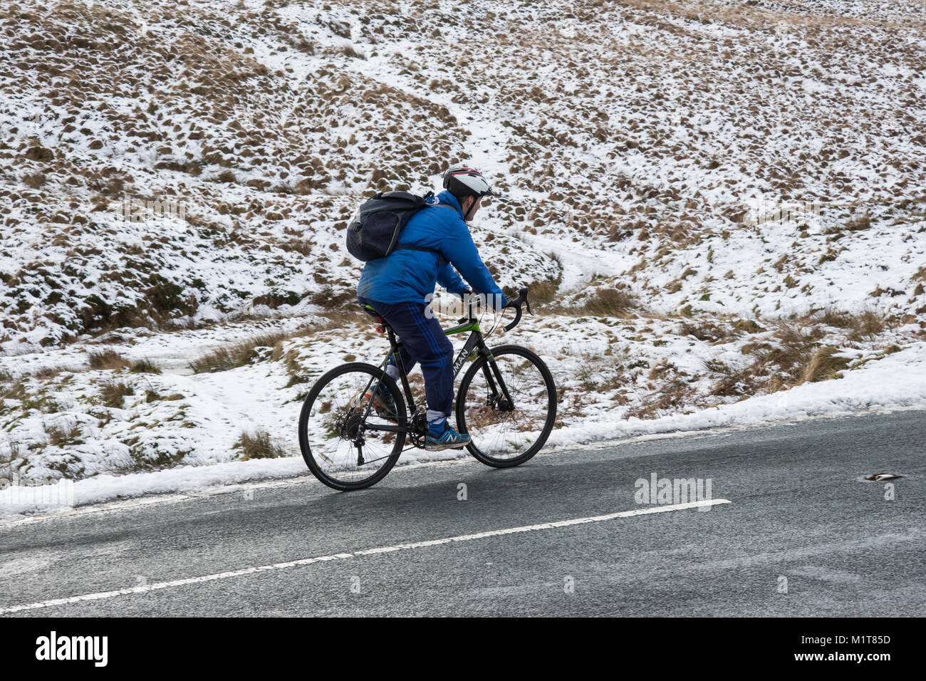 Ciclista solitario in condizioni di neve sul Yorkshire Moors sopra Marsden Foto Stock