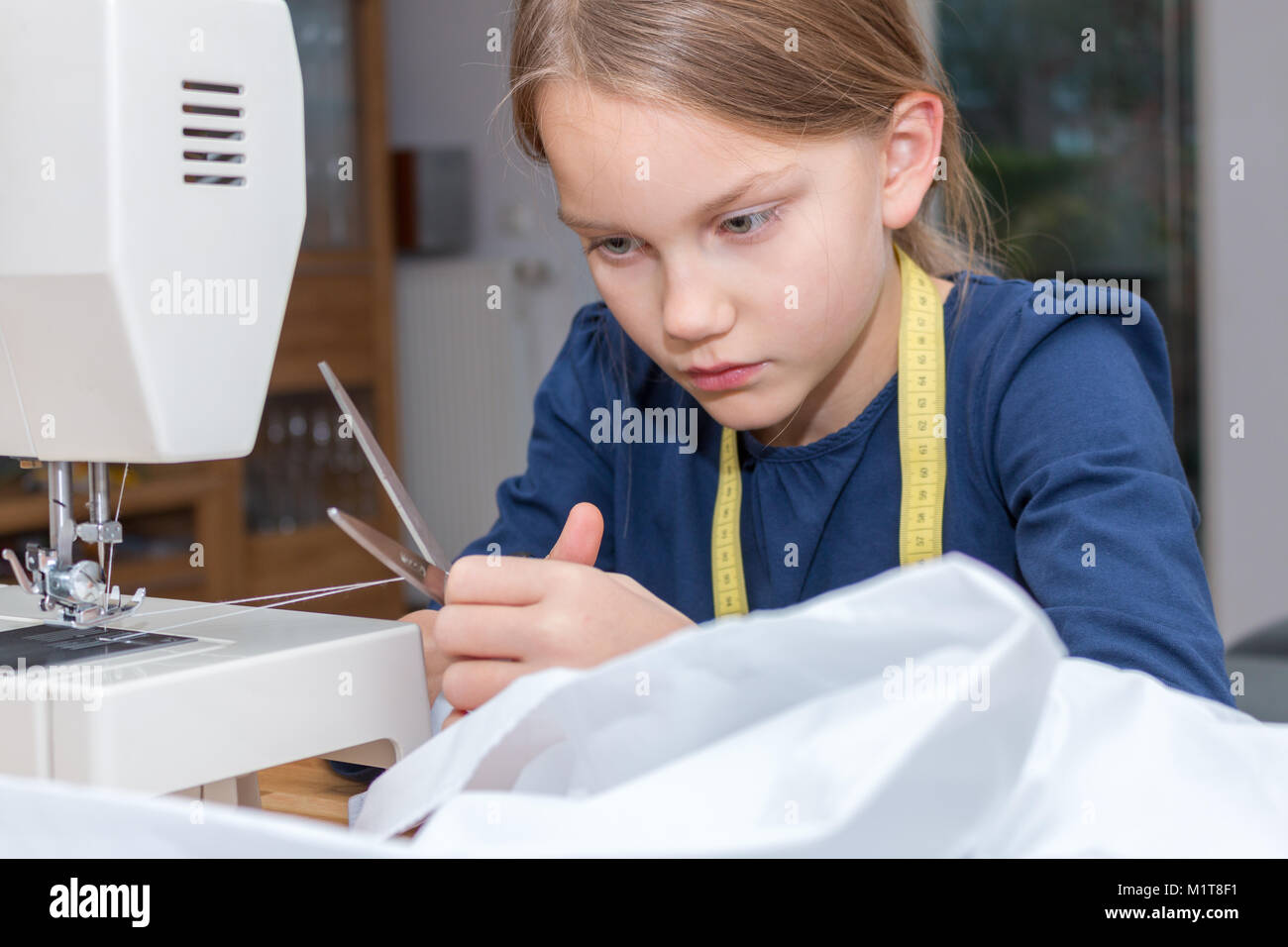 Una bimba di 8 anni, è filo di taglio del filato con le forbici Foto Stock