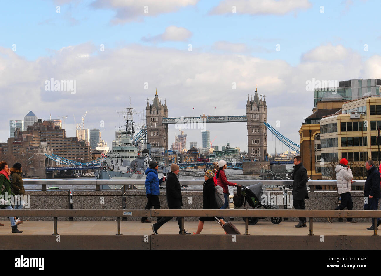 Un certo numero di cittadini e turisti pendolari camminando sul Ponte di Londra con il Tower Bridge e HMS Belfast in background sul fiume Tamigi a Londra. Foto Stock