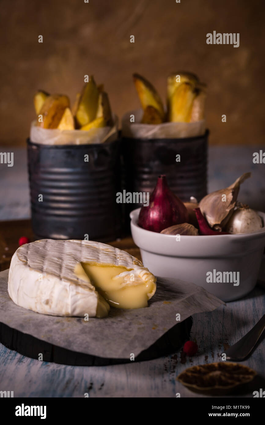 Foto verticale di fuso a caldo di formaggio camembert sul pezzo di carta e vintage tavola di legno con ciotola piena di colori le cipolle e gli spicchi d aglio e fritto po Foto Stock