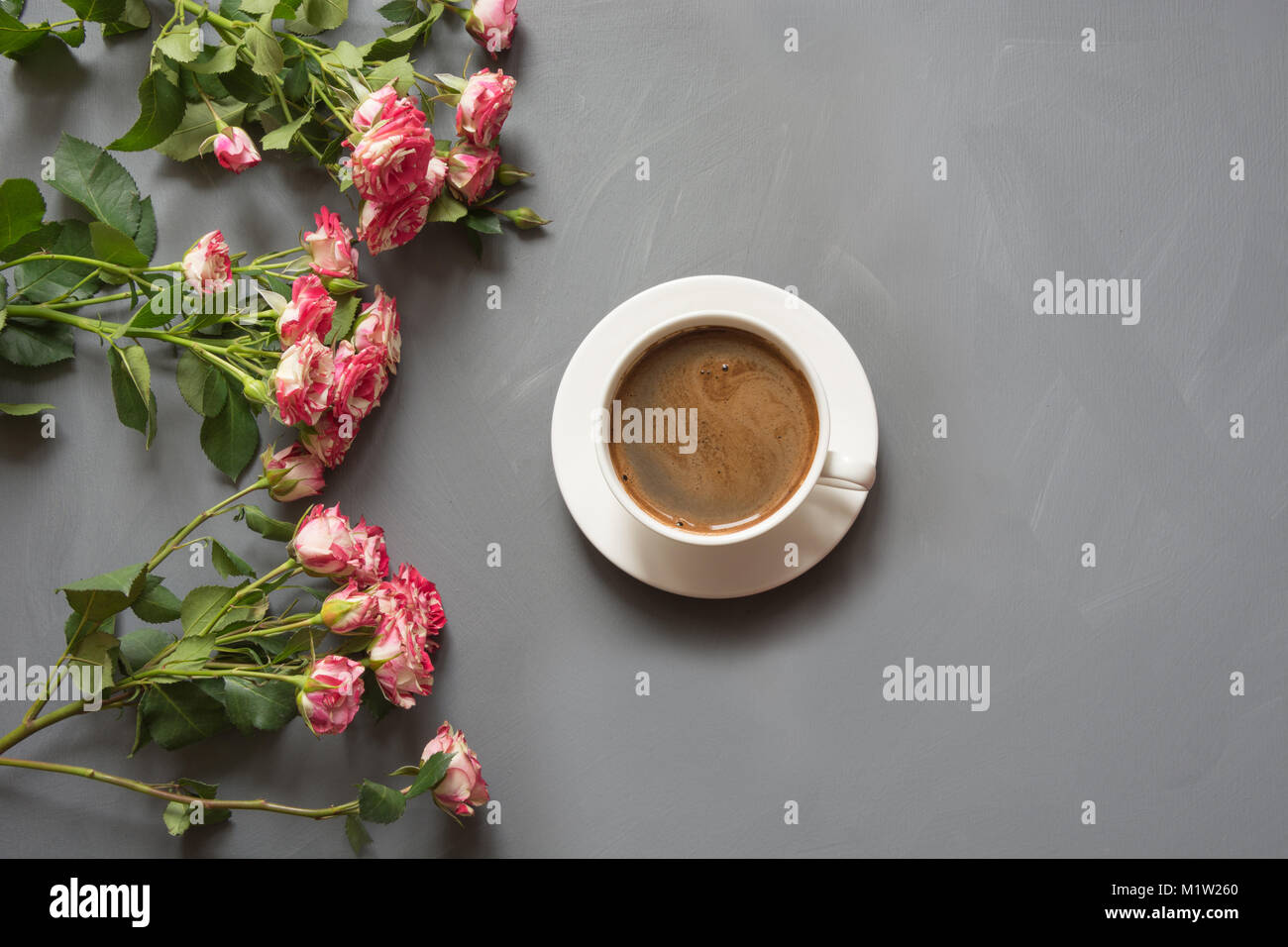 Profumo di rosa rose bush e la tazza di caffè sul shabby chic lo sfondo grigio, alto punto di vista. Copia dello spazio. Foto Stock