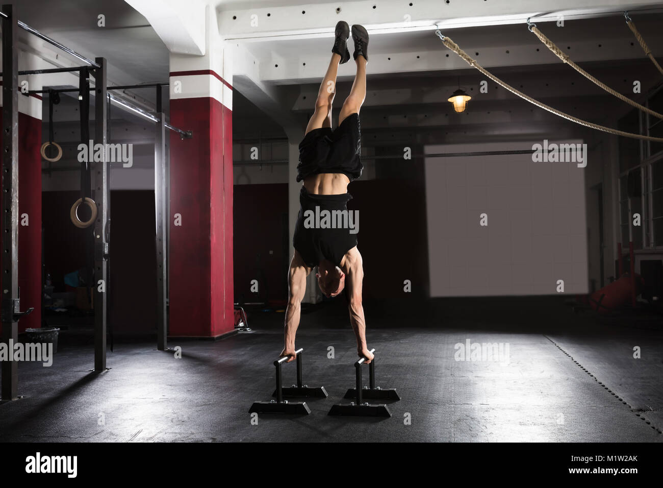 Atleta giovane uomo che fa Handstand esercitare sulla barra parallela in palestra Foto Stock