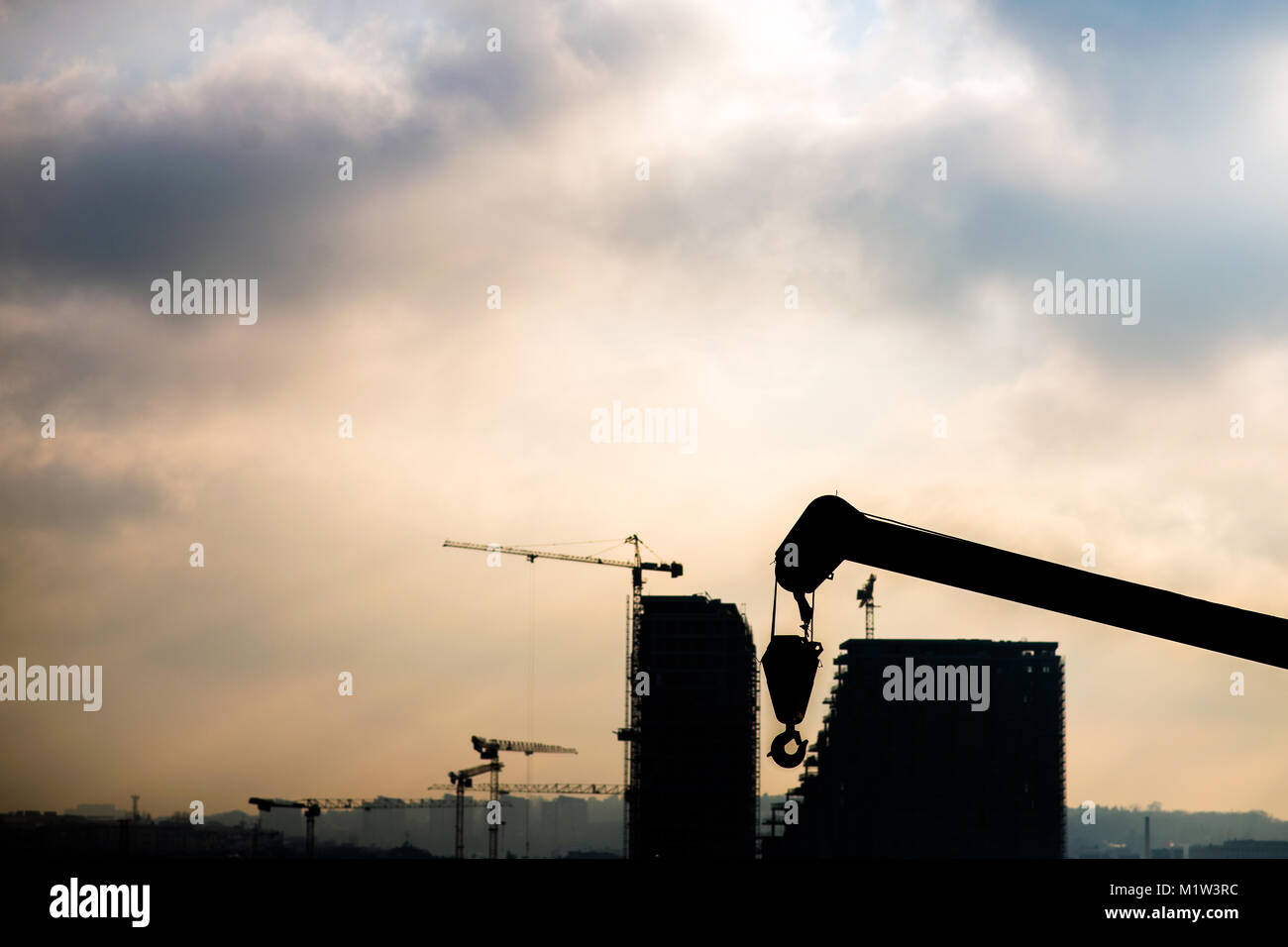 La costruzione di un edificio moderno. Silhouette di macchine e gru lavorando su un sito in costruzione Foto Stock