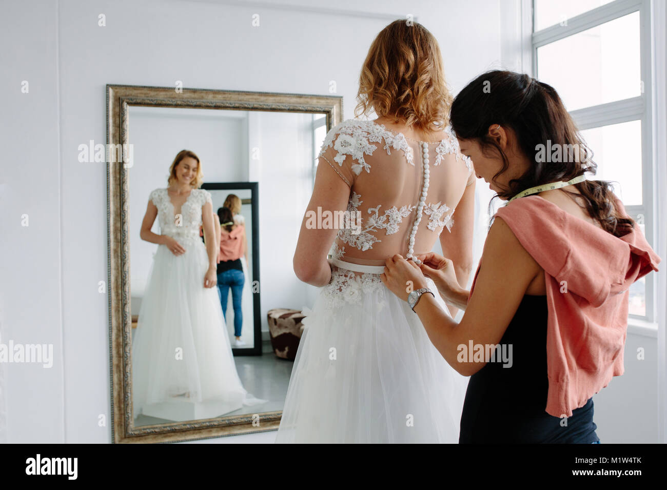 Assistente donna aiutando femmina cercando in abito da sposa in un negozio. Bridal shop proprietario assistere giovane sposa di vestirsi in abito da sposa. Foto Stock