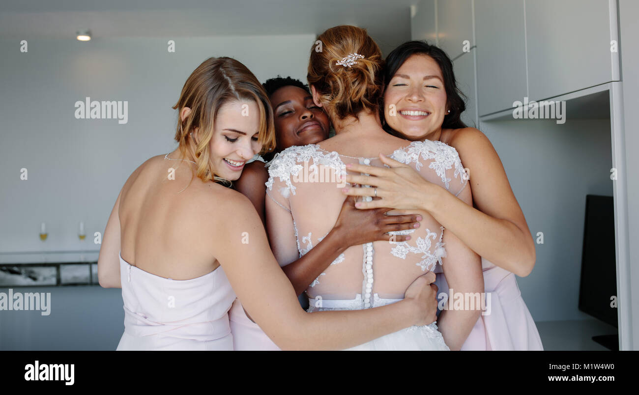 Allegro bridesmaids abbracciando sposa abito da sposa in camera d'albergo. Giorno di nozze, felice bridesmaids congratularmi con la sposa e sorridente. Foto Stock