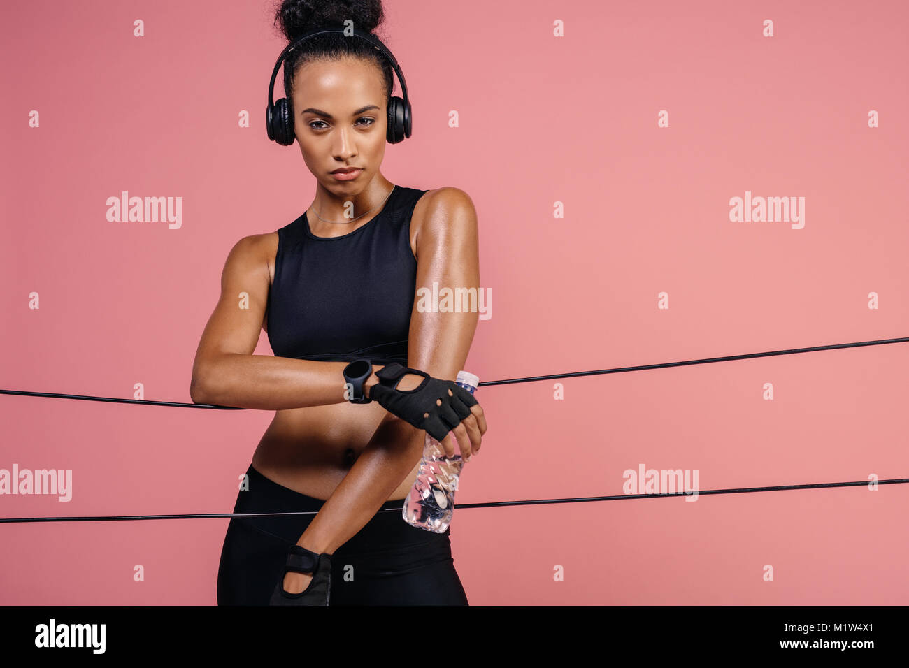 Donna Fitness con le cuffie e acqua in bottiglia appoggiata su nastri di  gomma in studio. Femmina di prendere una pausa dopo aver esercitato con  bande di resistenza Foto stock - Alamy