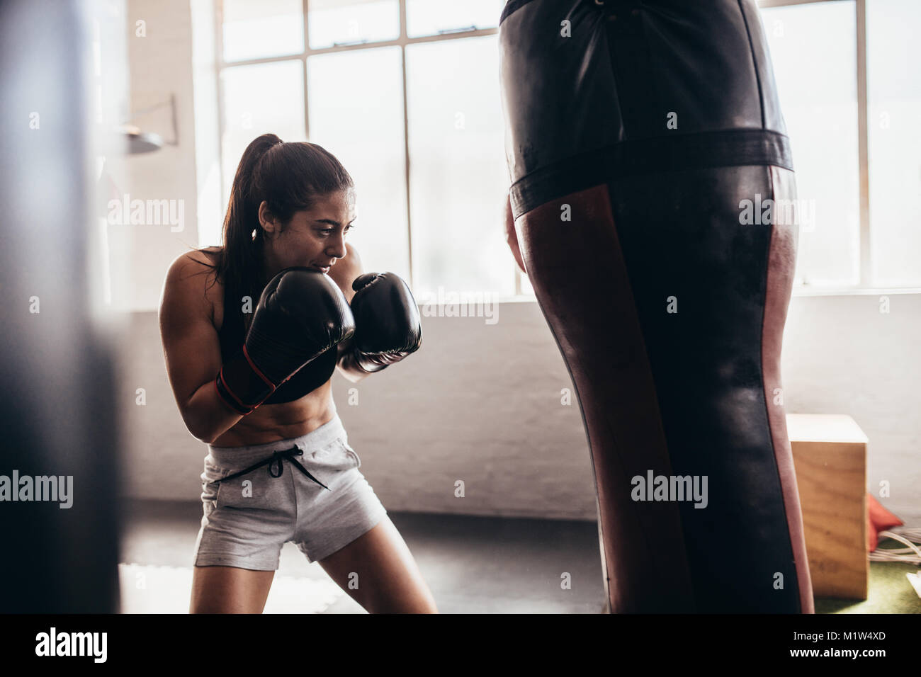 Boxer femmina di colpire un enorme sacco da boxe presso un studio di inscatolamento. Donna boxer allenamento duro. Foto Stock