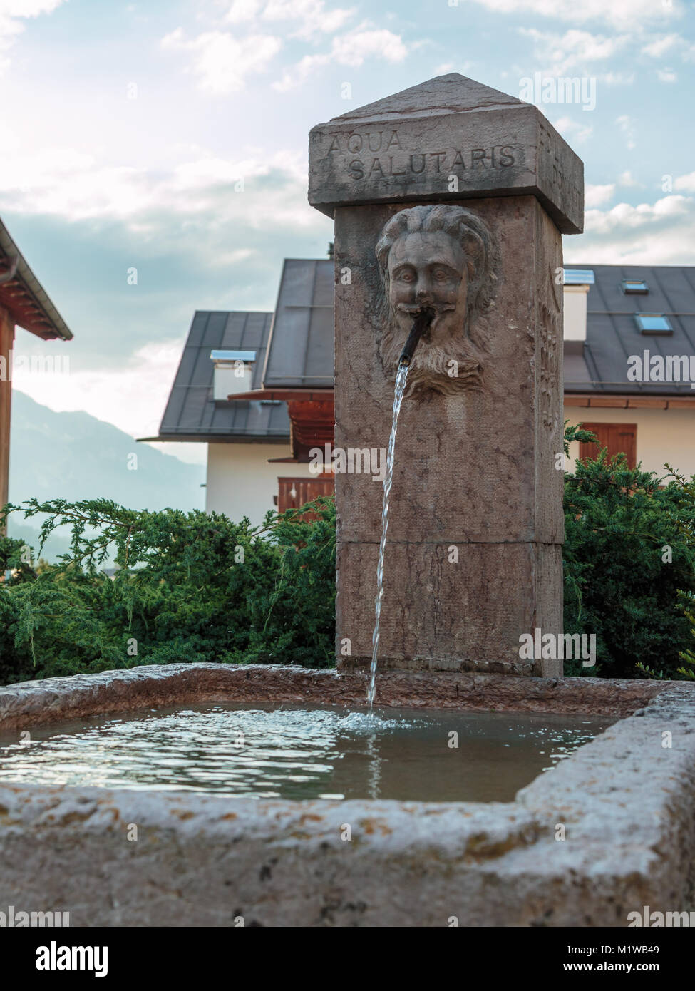 Fontana pubblica con testo latino in montagna villaggio tra case Foto Stock