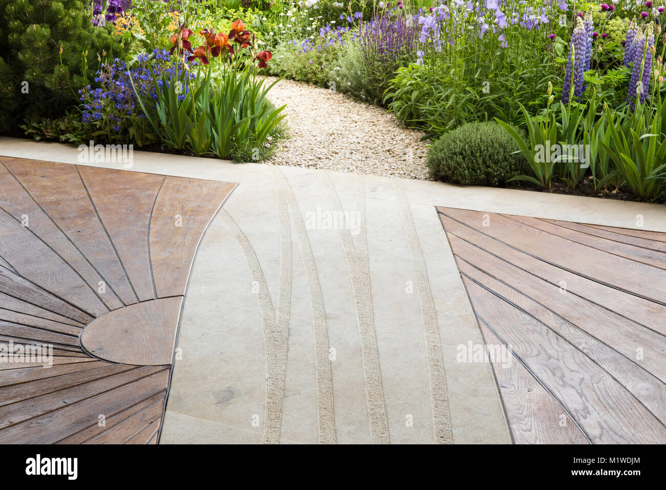 Moderno e contemporaneo patio in legno ponte di legno con percorso curvo in ghiaia giardino che conduce attraverso un cottage giardino selvaggio, Chelsea Flower show UK Foto Stock