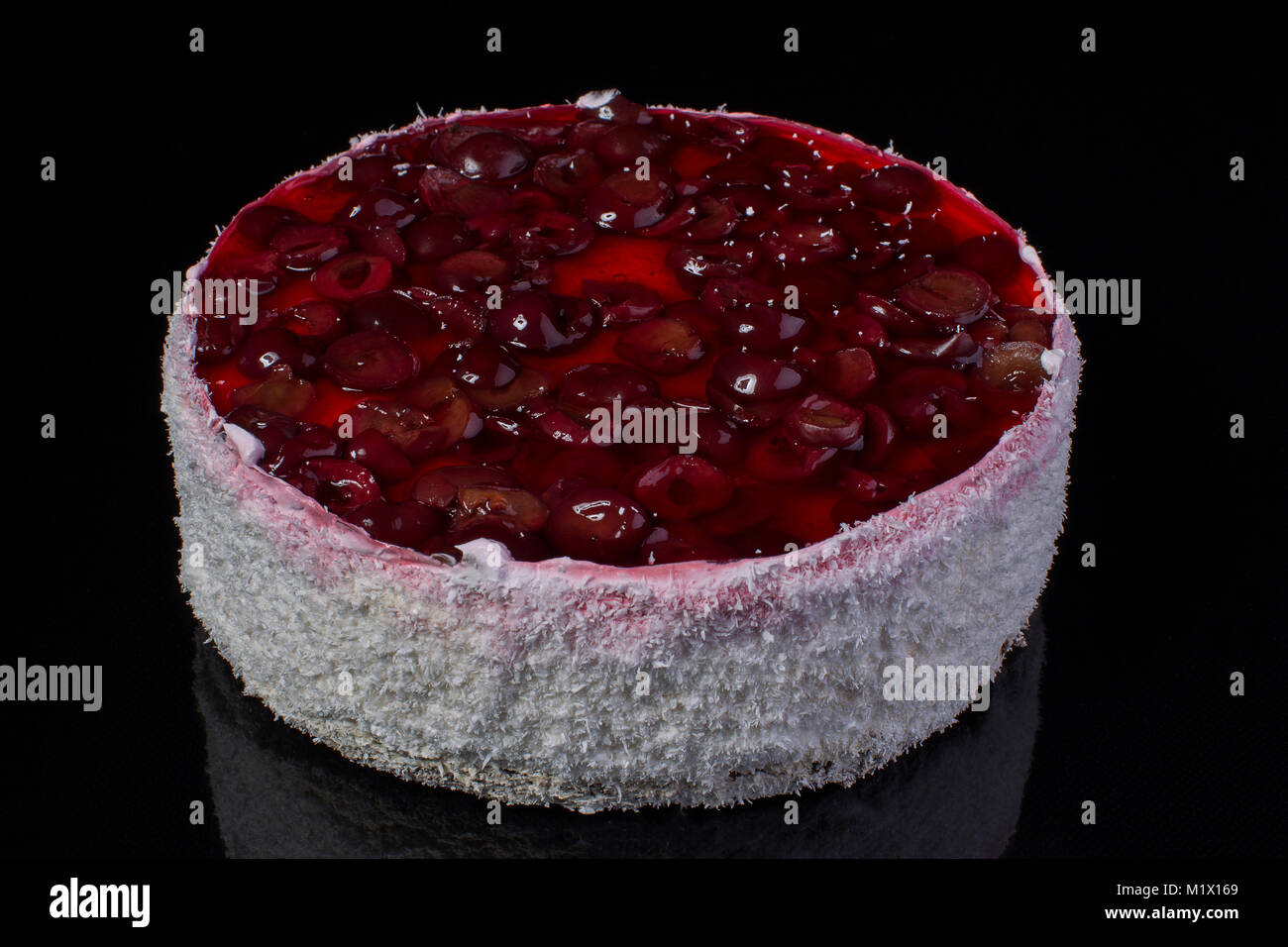 Grande torta in scaglie di noce di cocco con una ciliegia in jelly su sfondo nero Foto Stock