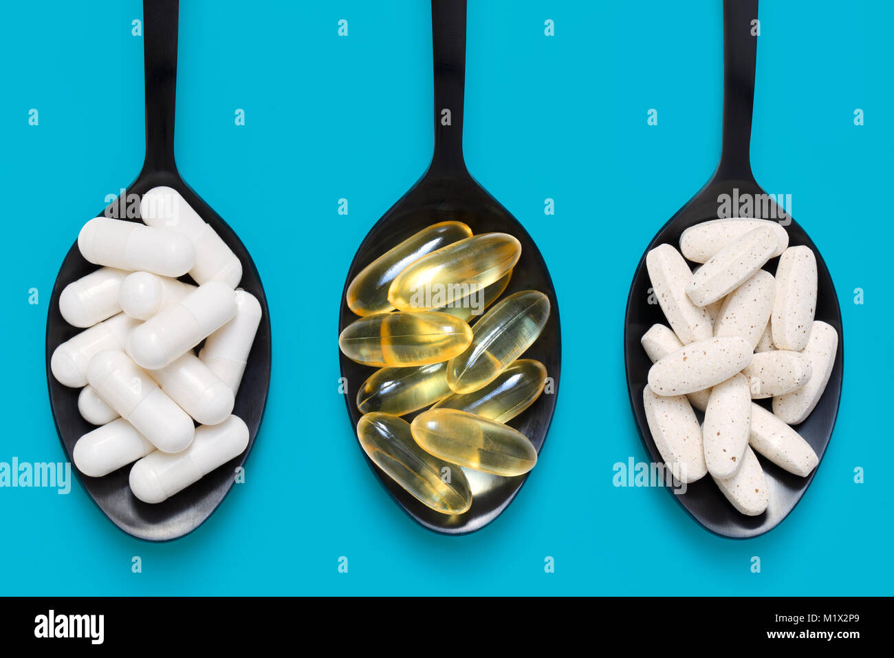 Vitamine e minerali e di vitamina D capsule su nero cucchiai contro uno sfondo colorato Foto Stock