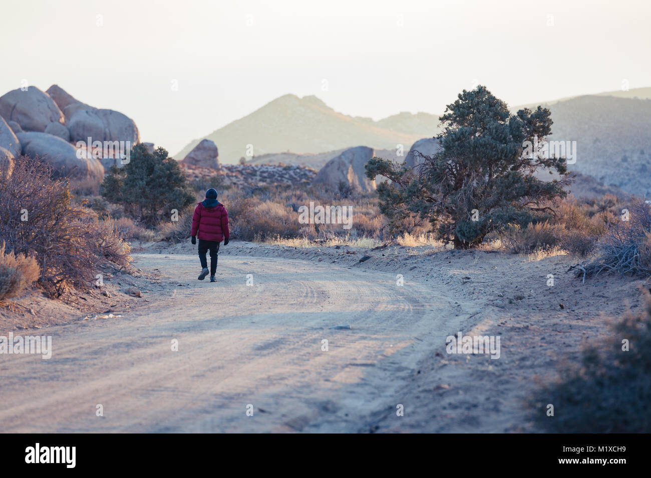 L'uomo vestito di freddo di abbigliamento passeggiate lungo un polveroso  sterrato nel deserto con enormi massi vicino Foto stock - Alamy