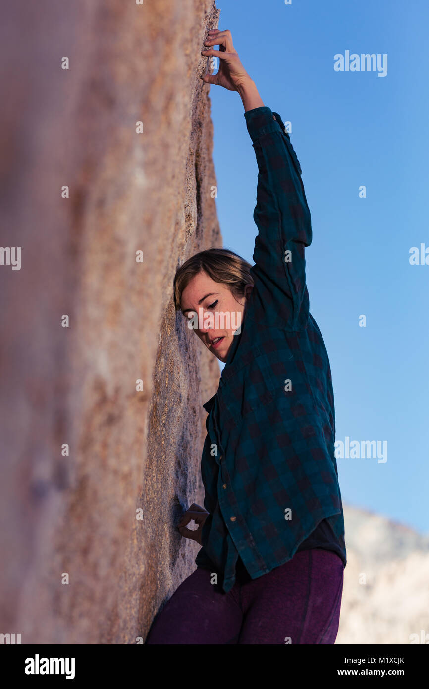 Sottile caucasico bionda donna che indossa flannel contro il freddo arrampicata su massi nel deserto della California Foto Stock