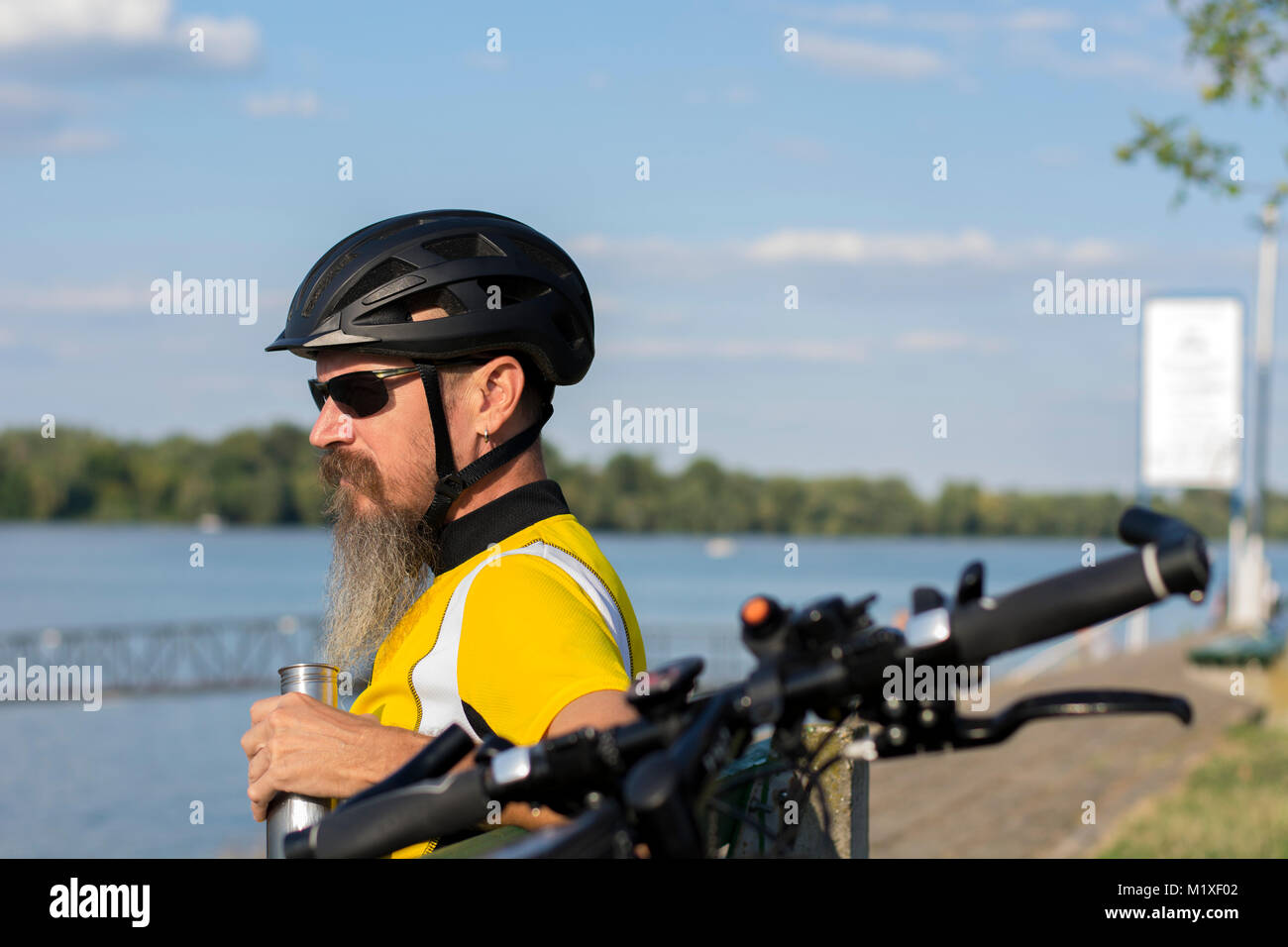 Ciclista tenendo a riposo su una panchina vicino al fiume Foto Stock