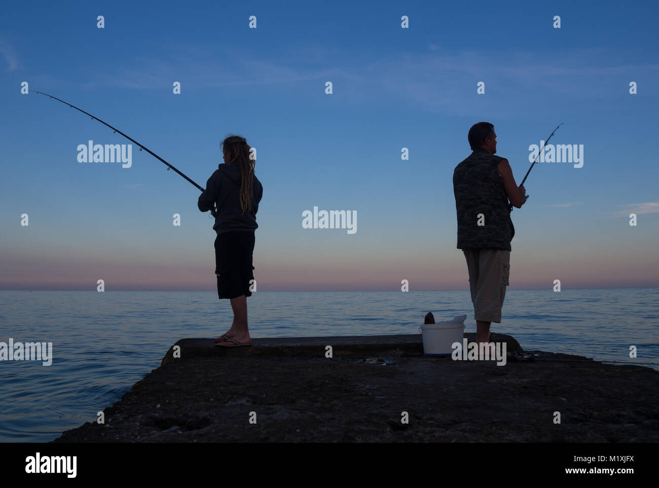 Gli uomini al tramonto per la cattura di pesci da esca dal molo Foto Stock