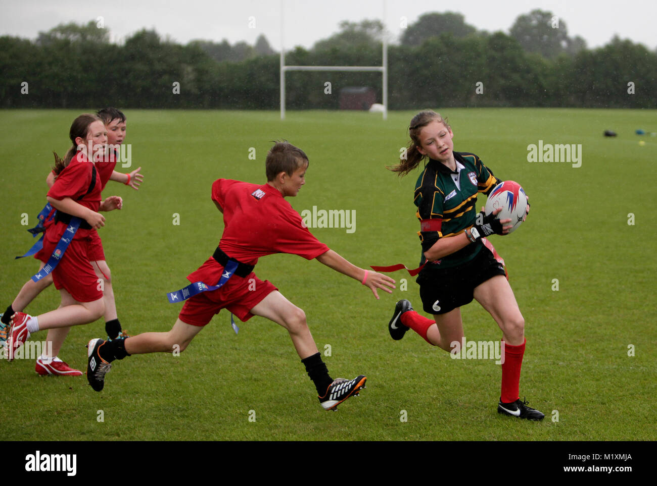 Ragazze e ragazzi giocando Tag Rugby nelle Midlands in un pomeriggio piovoso in primavera. Foto Stock