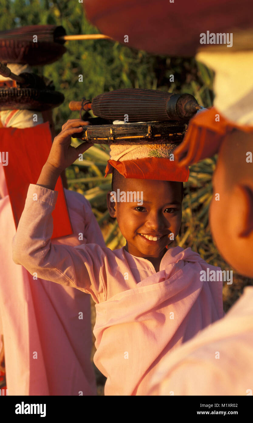Myanmar (Birmania). Bagan (pagano). Giovane buddista monache che porta ombrellone e la piastra sulla testa. La raccolta di cibo, ALMS. Foto Stock