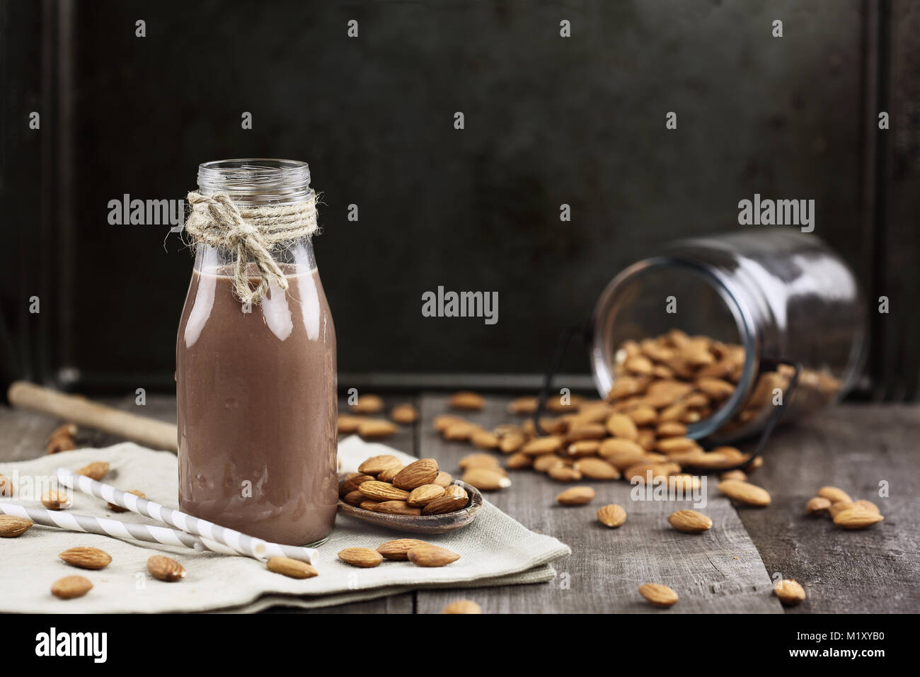 Cioccolato Bio latte di mandorla in una bottiglia di vetro con mandorle intere rovesciato sopra una tavola in legno rustico. Foto Stock