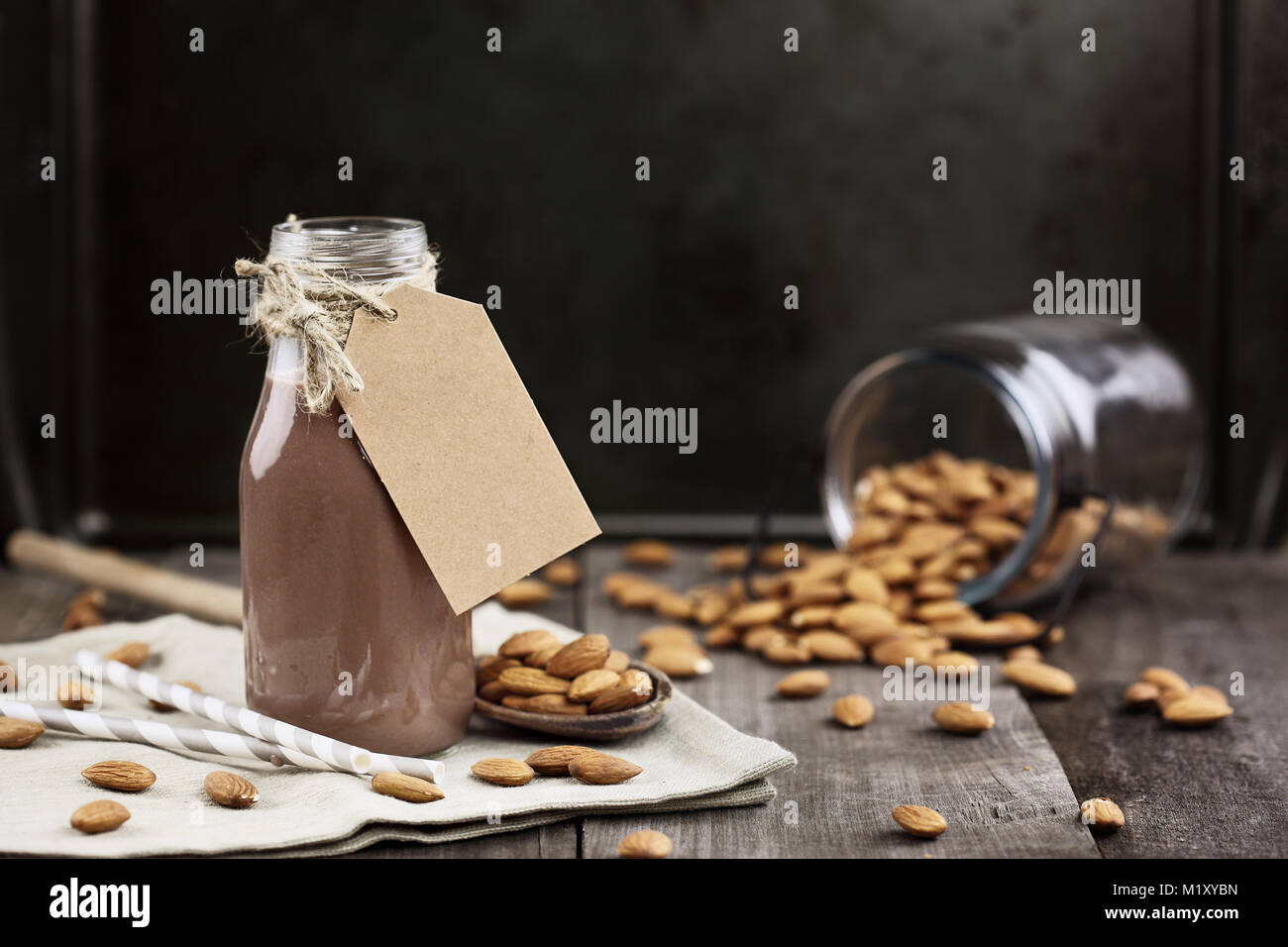 Organici di cioccolato al latte di mandorla con tag in una bottiglia di vetro con mandorle intere rovesciato sopra una tavola in legno rustico. Foto Stock