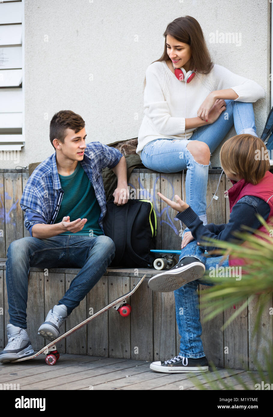 Tre sorridenti adolescente amici appendere fuori all'aperto e a discutere di qualcosa. Focus su guy Foto Stock