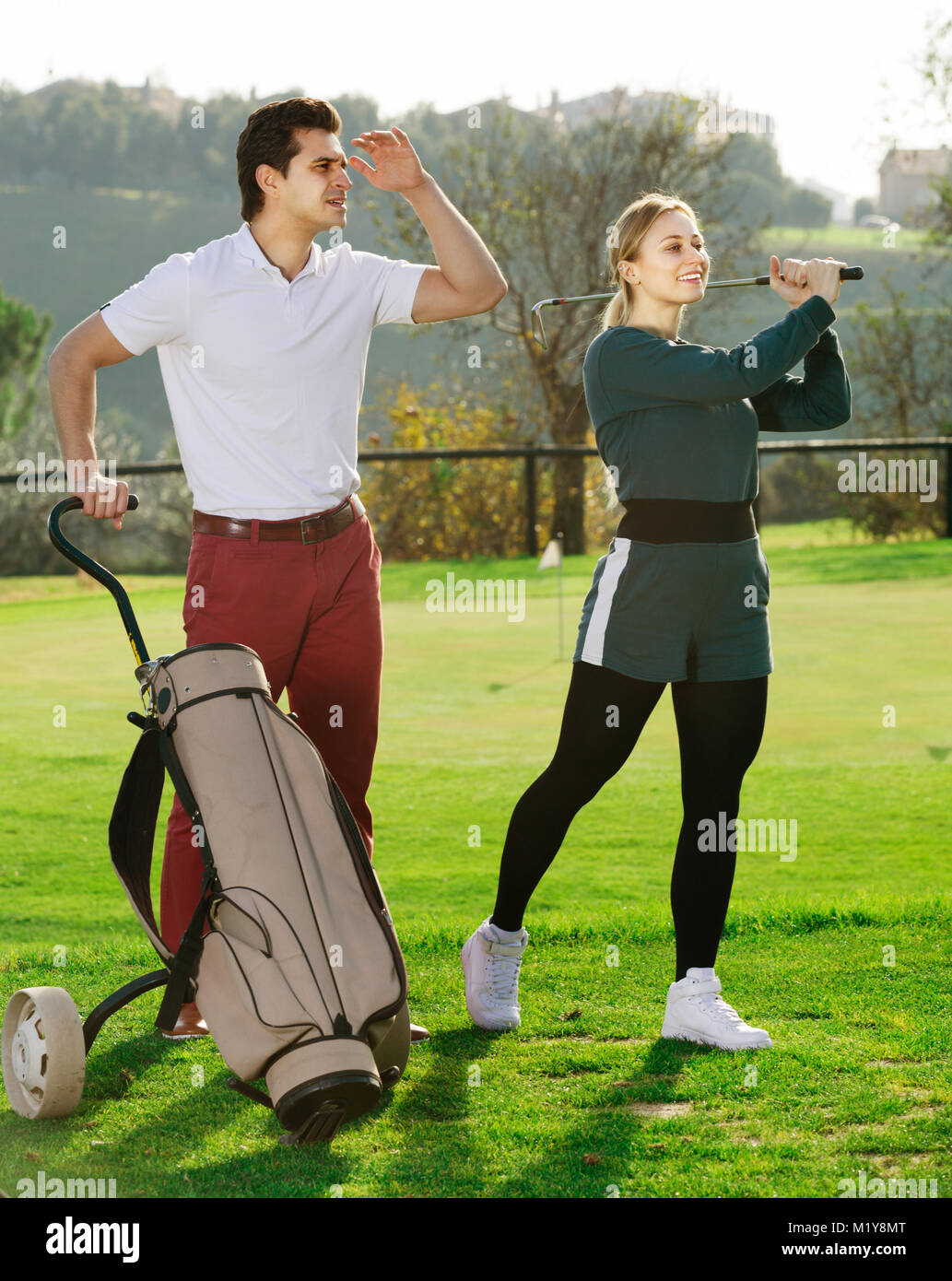 Giovane maschio è che mostra una donna per giocare a golf e colpire la sfera correttamente. Foto Stock