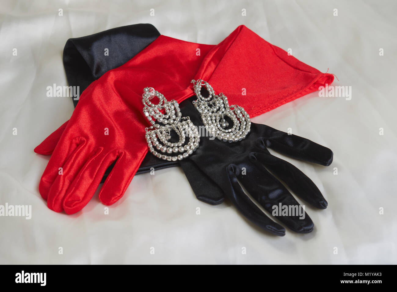 Due incantevoli rosso e guanti neri accanto ad alcuni orecchini brillante su sfondo bianco Foto Stock