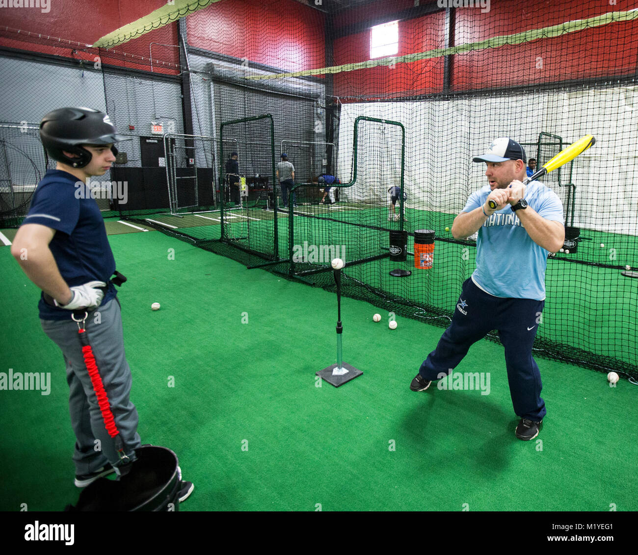 Il baseball coach dimostrando la corretta tecnica di colpire con un allenamento indoor facility in New Jersey Foto Stock