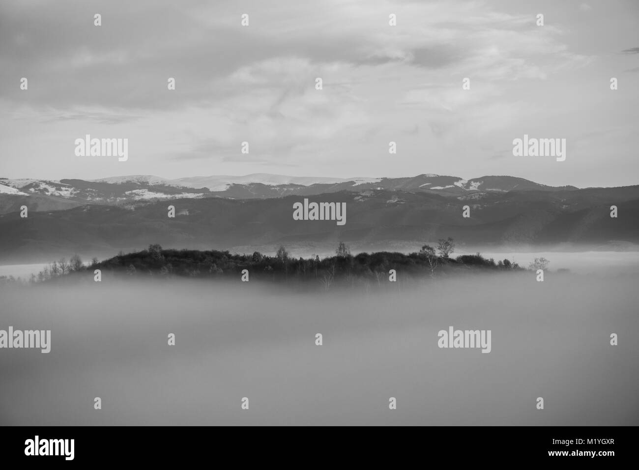 Bianco e nero colpo di piccola collina forando la fitta nebbia che ha travolto la valle al di sotto di Foto Stock