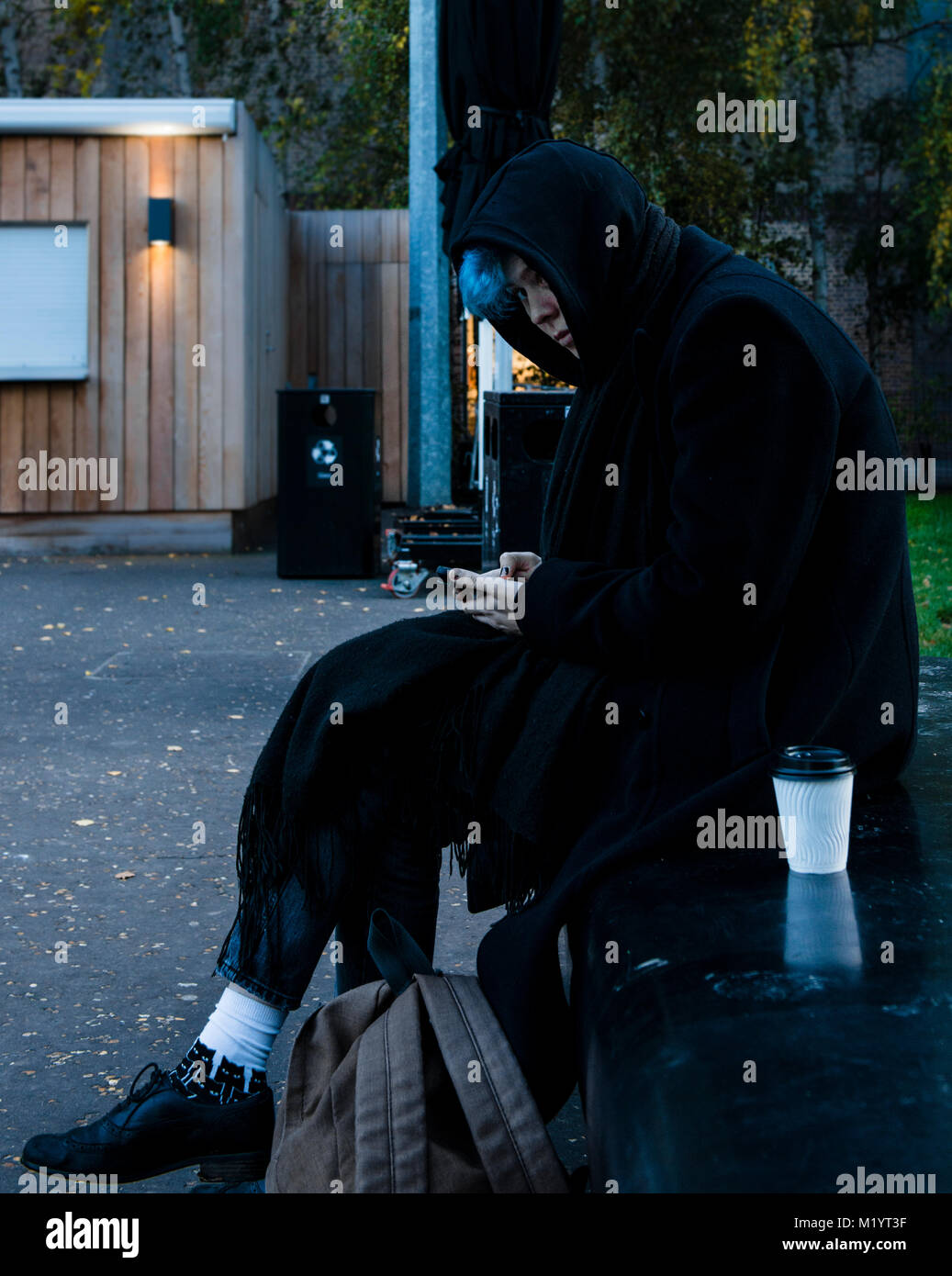 Persona seduta sul banco indossando cappotto con cappuccio, la Tate Modern di Londra, Inghilterra Foto Stock