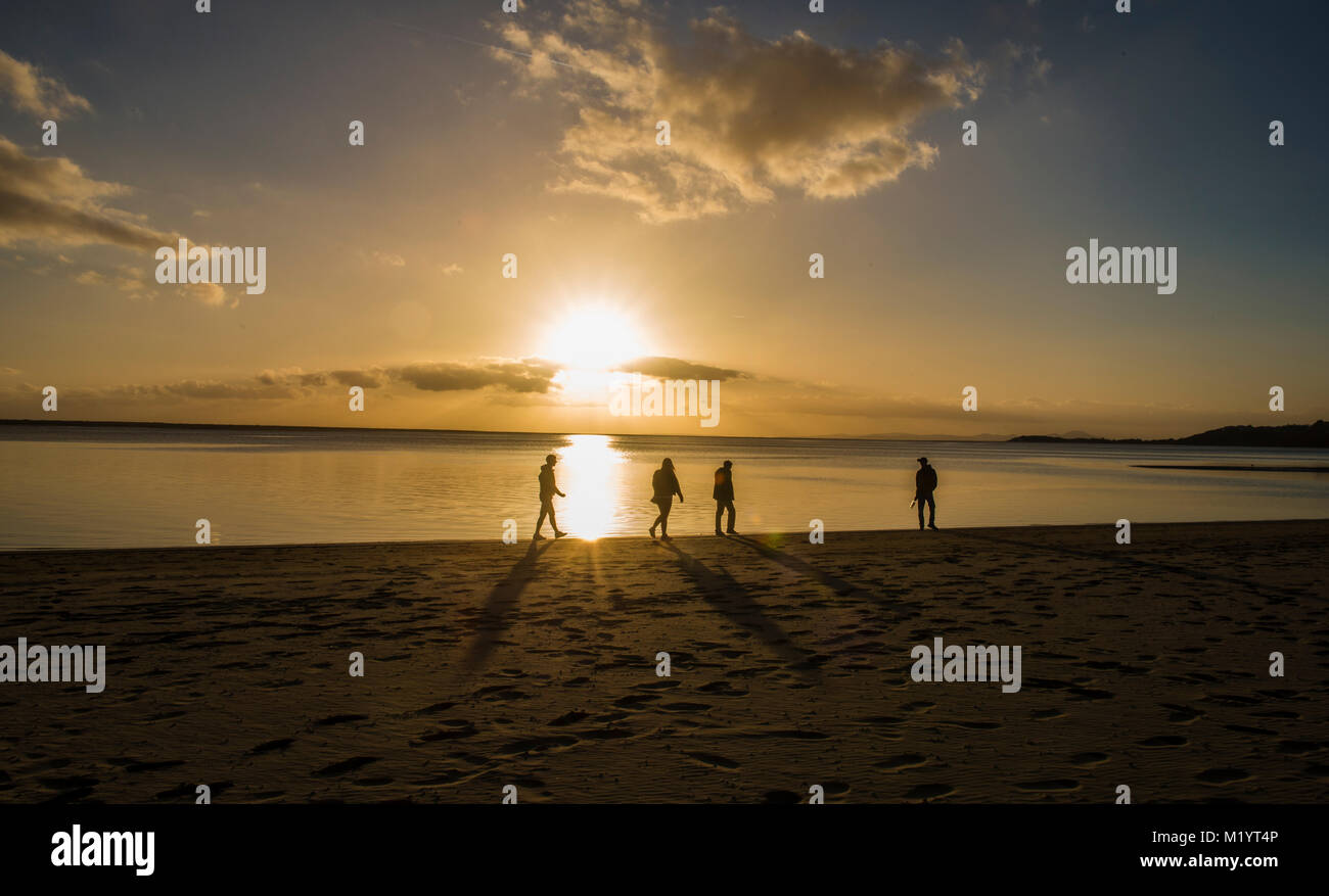Quattro persone camminando sulla spiaggia al tramonto Foto Stock