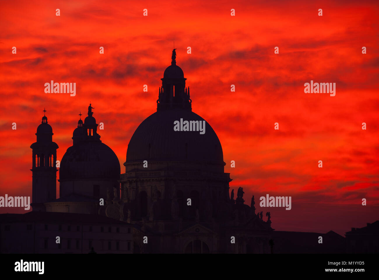 Rosso Sangue sky tramonto sulla laguna di Venezia con la Basilica salutano cupole Foto Stock