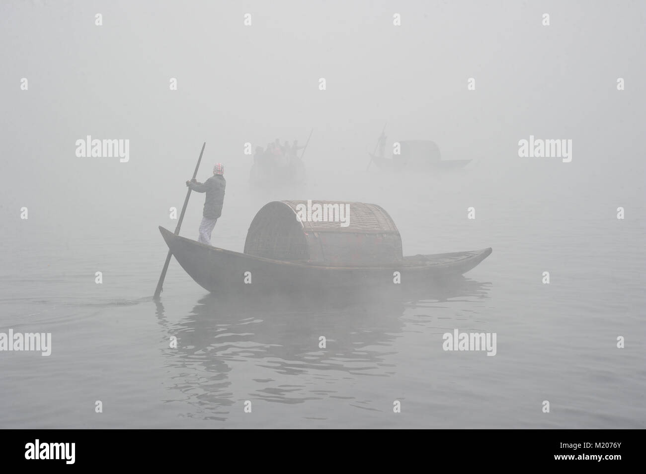 Barca uomini guida della loro barca con i passeggeri in una fredda e nebbiosa mattina inverno sul fiume Shitalokha in Naraynganj, Bangladesh Foto Stock