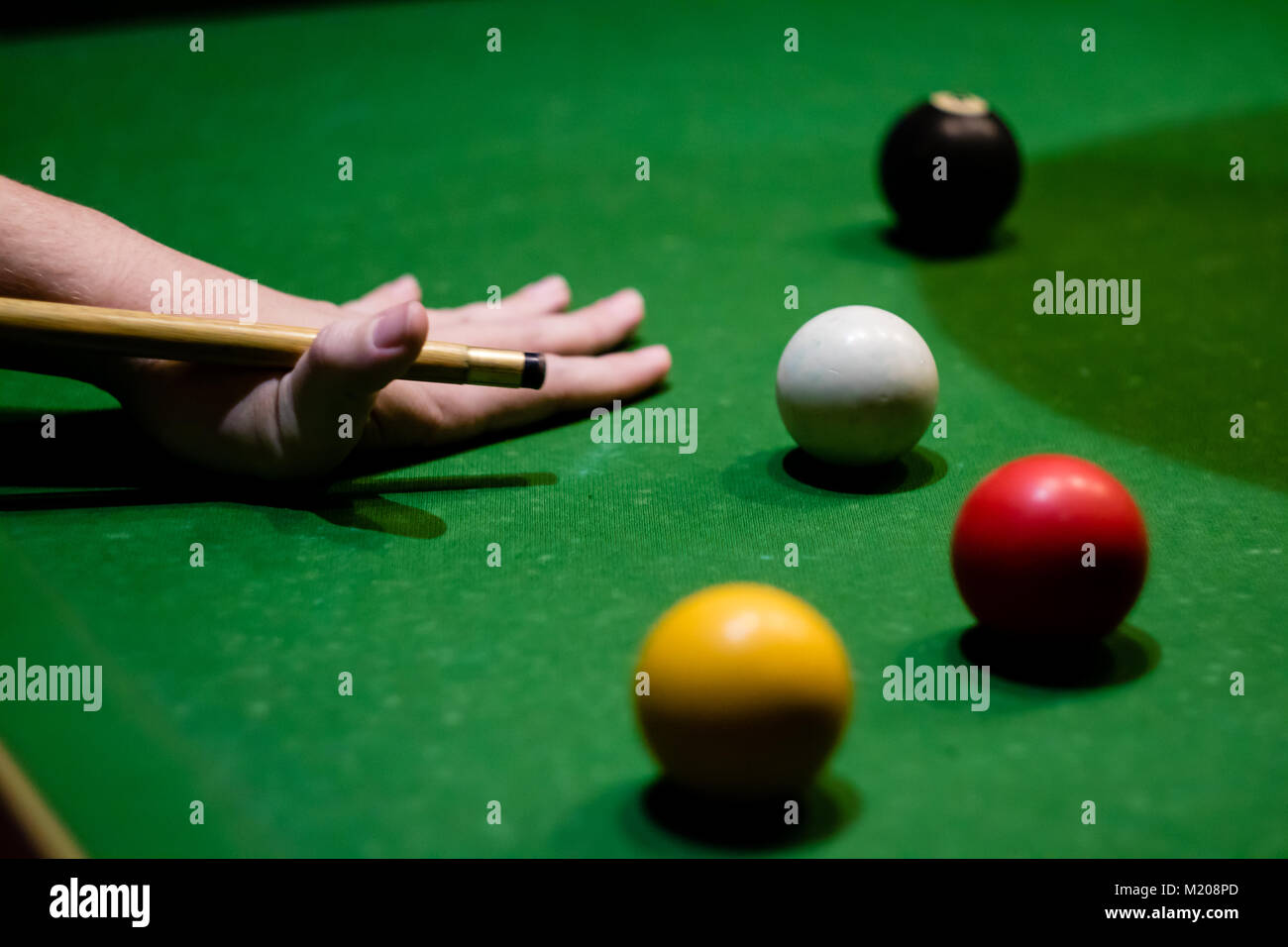 Una mano si preparano a svolgere un pool shot, con un rosso e giallo palla, la palla nera e la bilia battente tutte visibili. Foto Stock