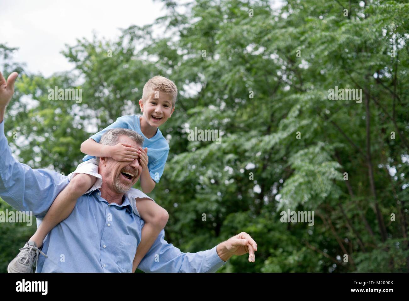 Nonno nipote che porta sulle spalle, ragazzo di copertura del nonno gli occhi con le mani. Foto Stock