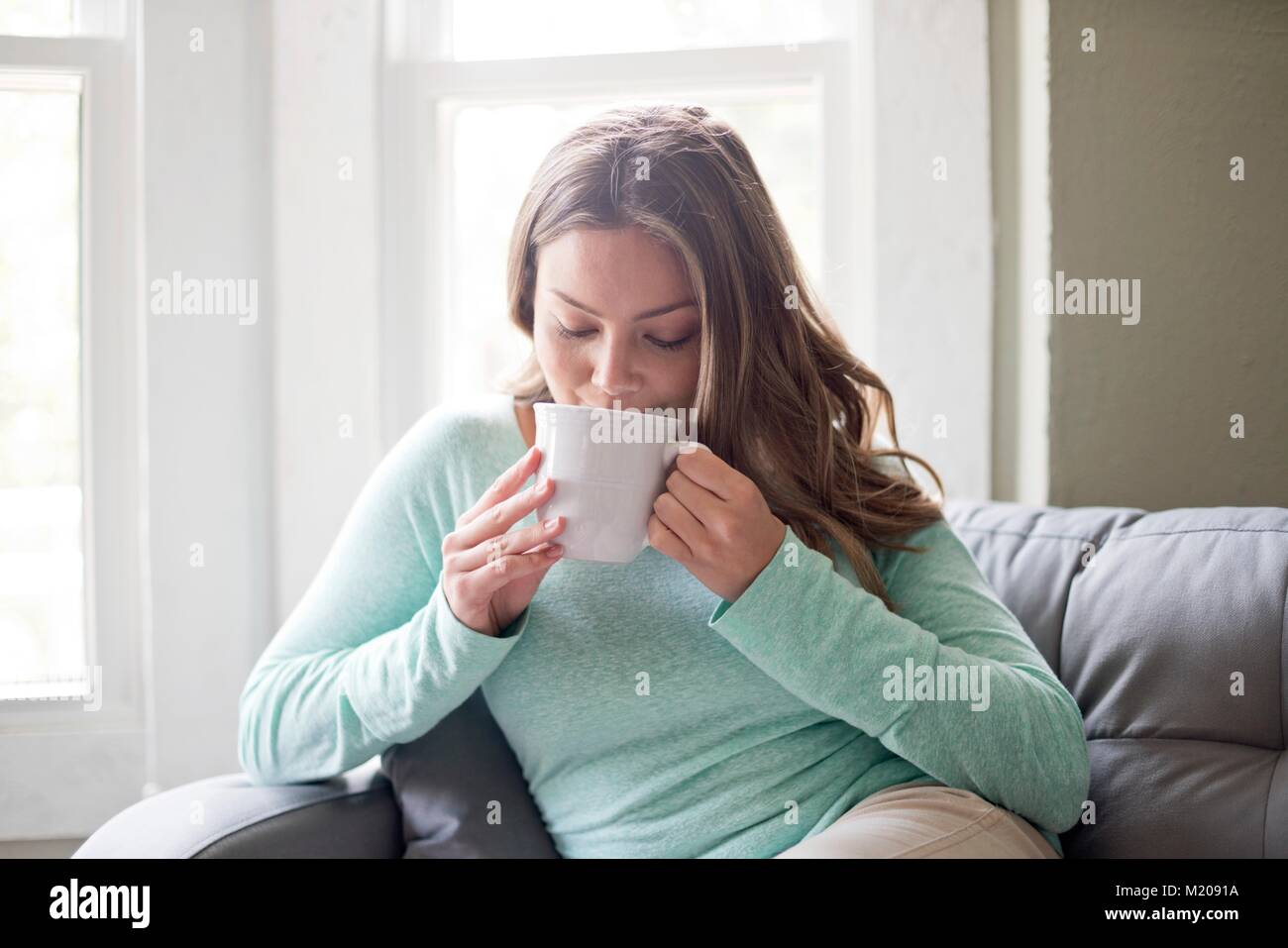 Giovane donna di bere una bevanda calda da una tazza alta. Foto Stock