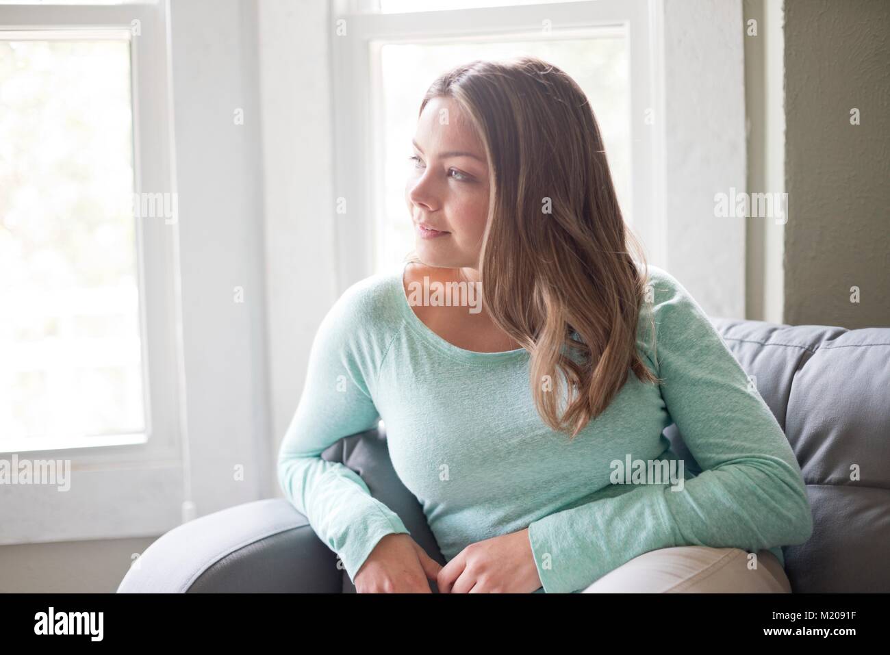Giovane donna seduta sul divano e guardando lontano. Foto Stock