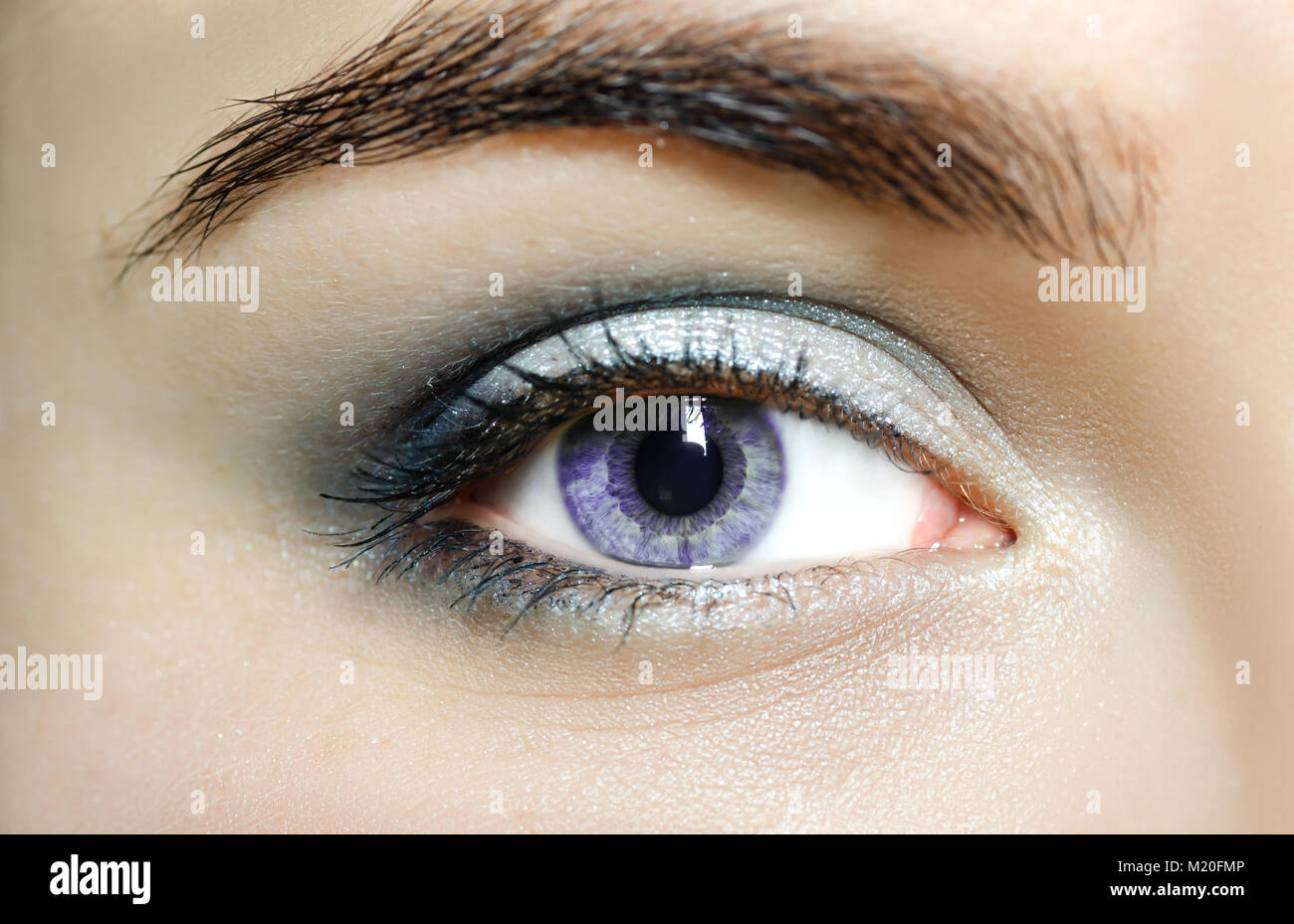 Occhi viola (mutazione occhi), vicino. L'occhio umano di una donna con luce di bellezza e cosmetici naturali lunghe ciglia. Ragazza con una pelle perfetta. Foto Stock