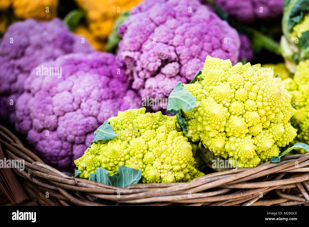 Organici colorati di verdure fresche in scatole di legno visualizzati al mercato. Verde vivace romanesco broccoli, viola e arancione cavolfiore al mercato in stallo. Foto Stock